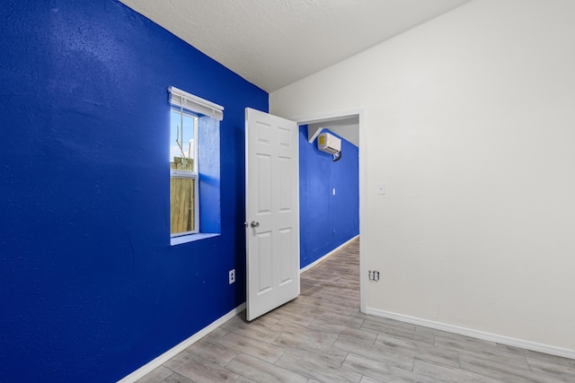 empty room featuring a wall mounted air conditioner, vaulted ceiling, light hardwood / wood-style floors, and a textured ceiling