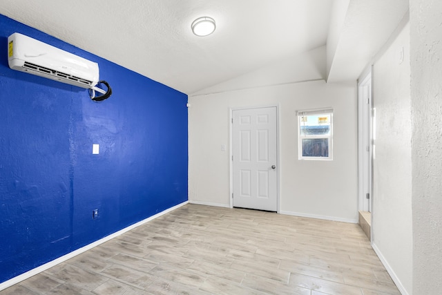 spare room with an AC wall unit, lofted ceiling, a textured ceiling, and light hardwood / wood-style flooring