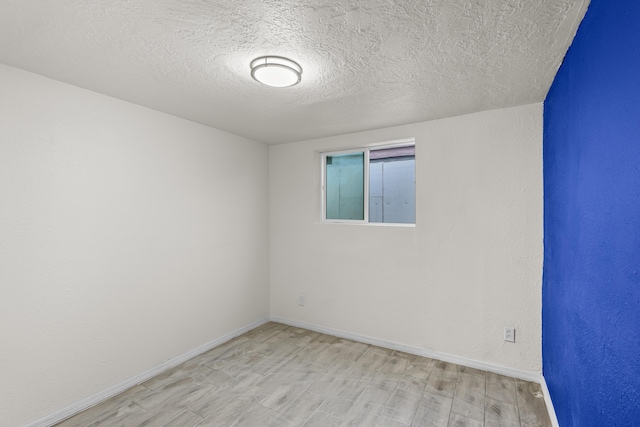 spare room featuring a textured ceiling and light hardwood / wood-style floors