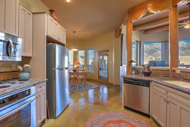 kitchen with appliances with stainless steel finishes, sink, white cabinets, dark stone counters, and hanging light fixtures