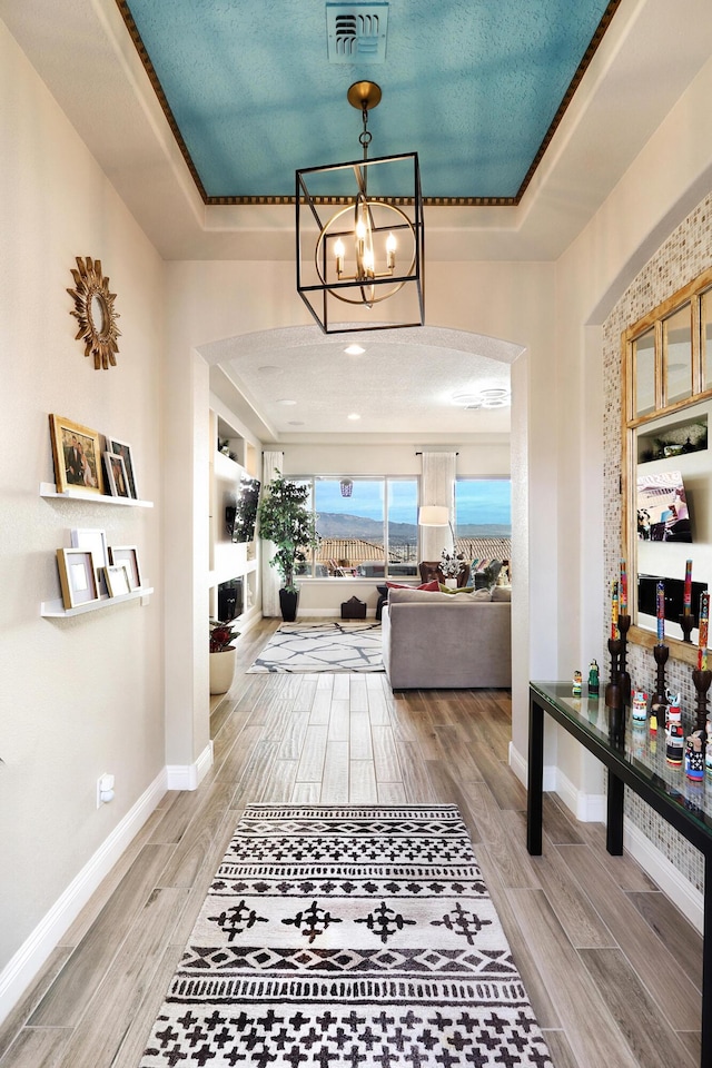 hall featuring an inviting chandelier and a raised ceiling