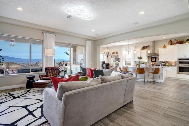 living room featuring sink, an inviting chandelier, light hardwood / wood-style floors, a textured ceiling, and a mountain view