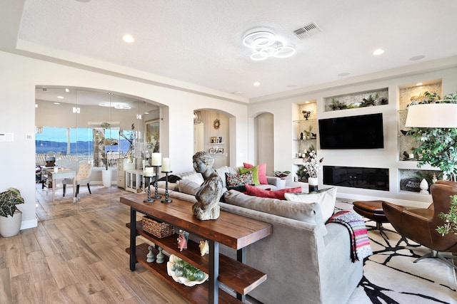 living room featuring built in features, light hardwood / wood-style floors, and a textured ceiling