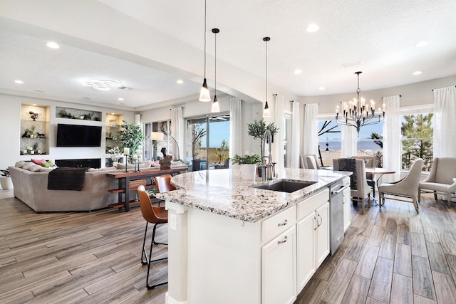 kitchen featuring white cabinetry, sink, hanging light fixtures, light stone countertops, and a center island with sink