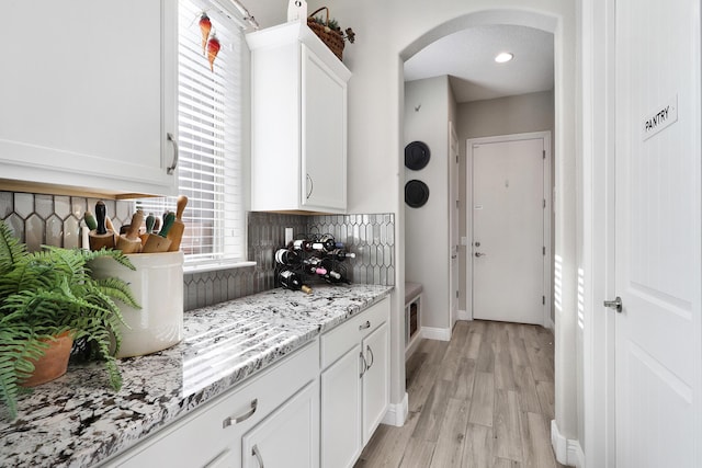 bar with tasteful backsplash, light wood-type flooring, white cabinets, and light stone counters