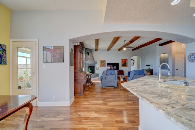 kitchen with light stone counters, beam ceiling, sink, and light wood-type flooring