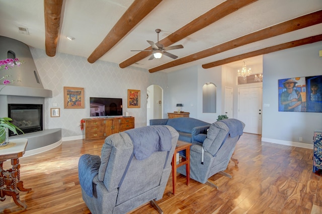 living room featuring ceiling fan with notable chandelier, wood-type flooring, a large fireplace, and beamed ceiling