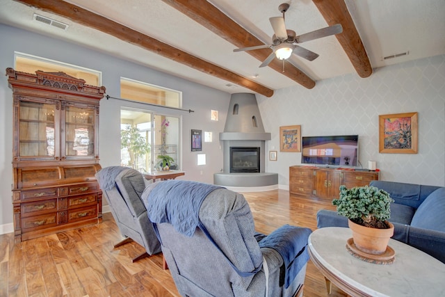 living room with ceiling fan, a large fireplace, beam ceiling, and light hardwood / wood-style flooring