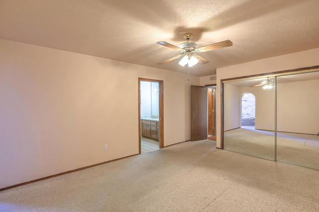 unfurnished bedroom with ensuite bath, ceiling fan, a textured ceiling, light colored carpet, and a closet