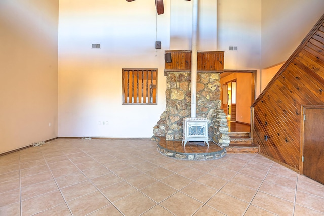 unfurnished living room featuring a high ceiling, light tile patterned flooring, ceiling fan, and a wood stove