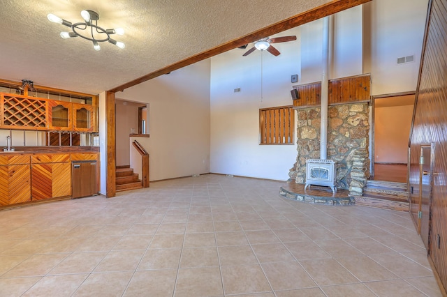 unfurnished living room featuring ceiling fan, a wood stove, light tile patterned floors, and a textured ceiling