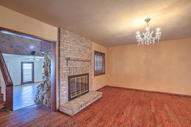 unfurnished living room with hardwood / wood-style flooring, a fireplace, a textured ceiling, and a chandelier