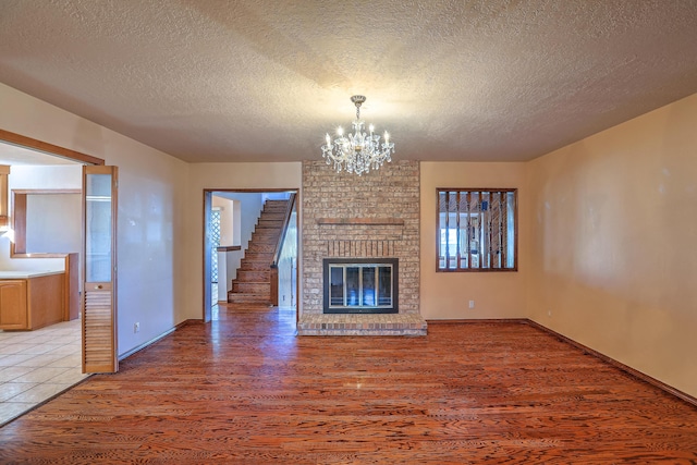 unfurnished living room with hardwood / wood-style flooring, an inviting chandelier, a textured ceiling, and a fireplace