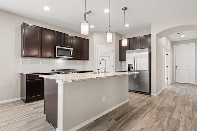 kitchen featuring sink, appliances with stainless steel finishes, a kitchen island with sink, hanging light fixtures, and dark brown cabinetry