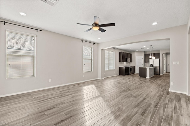 unfurnished living room with ceiling fan, a textured ceiling, and light wood-type flooring