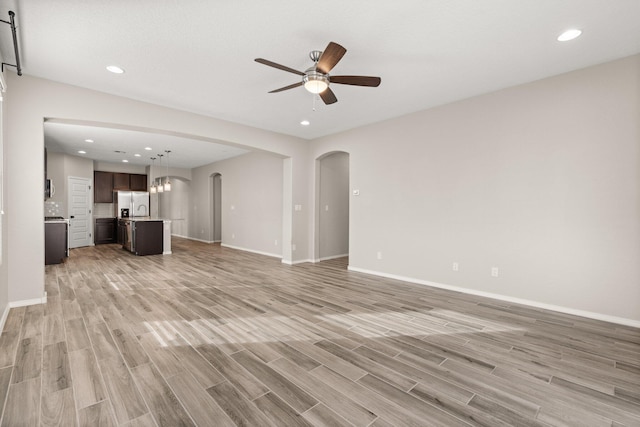 unfurnished living room featuring ceiling fan, a barn door, and light hardwood / wood-style floors