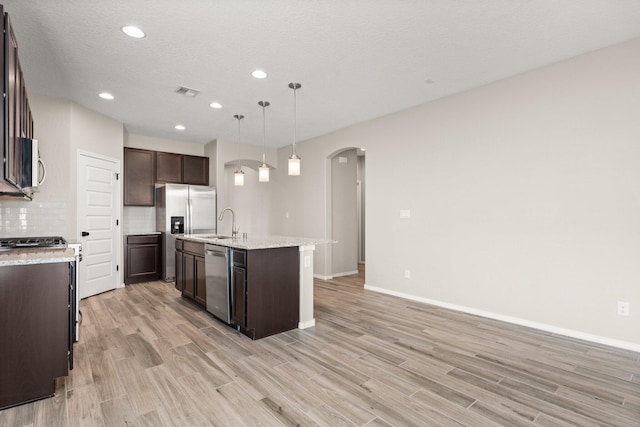 kitchen with tasteful backsplash, an island with sink, pendant lighting, stainless steel appliances, and light hardwood / wood-style floors