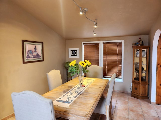 dining space with light tile patterned floors, arched walkways, and vaulted ceiling
