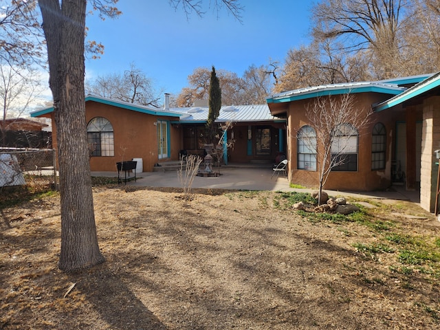 back of house with entry steps, metal roof, fence, stucco siding, and a patio area