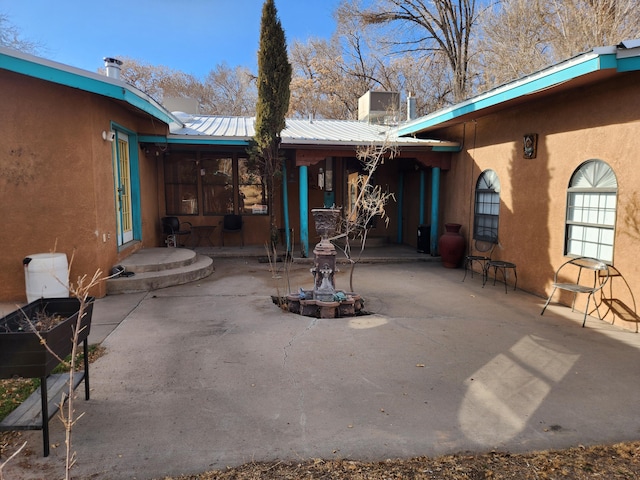 back of property featuring stucco siding, a chimney, metal roof, and a patio