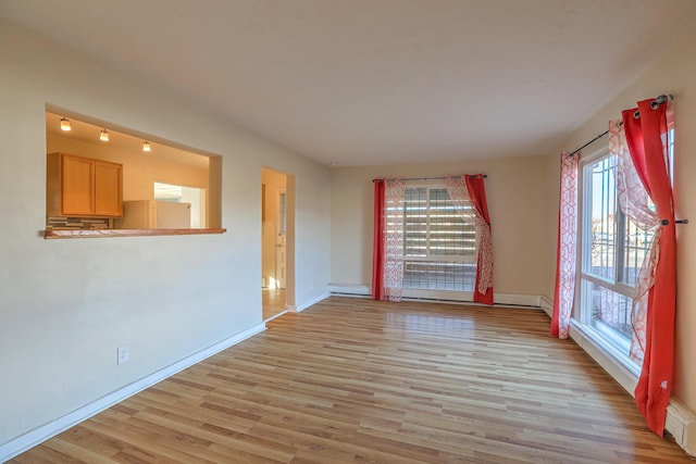 empty room with light wood-style floors, a baseboard radiator, and baseboards