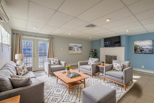 tiled living room with a paneled ceiling, baseboard heating, visible vents, and a healthy amount of sunlight