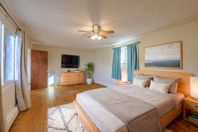 bedroom with a ceiling fan, a textured ceiling, baseboard heating, and wood finished floors