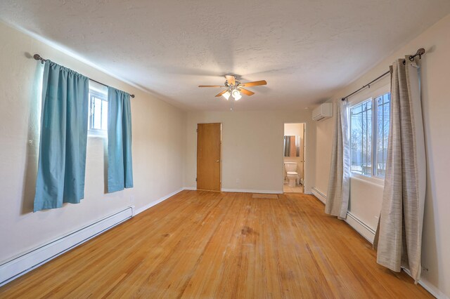 unfurnished room with a wall unit AC, light wood finished floors, a baseboard radiator, baseboard heating, and a textured ceiling