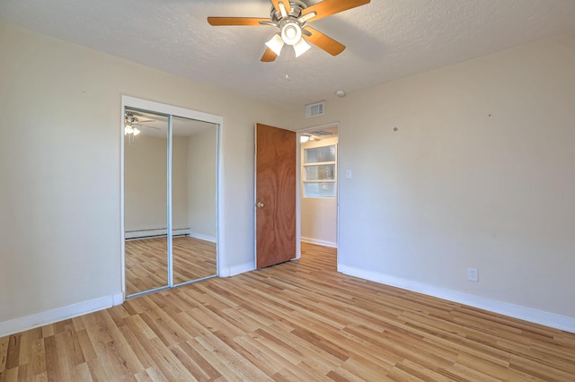 unfurnished bedroom featuring a baseboard radiator, a closet, visible vents, light wood-style flooring, and a textured ceiling