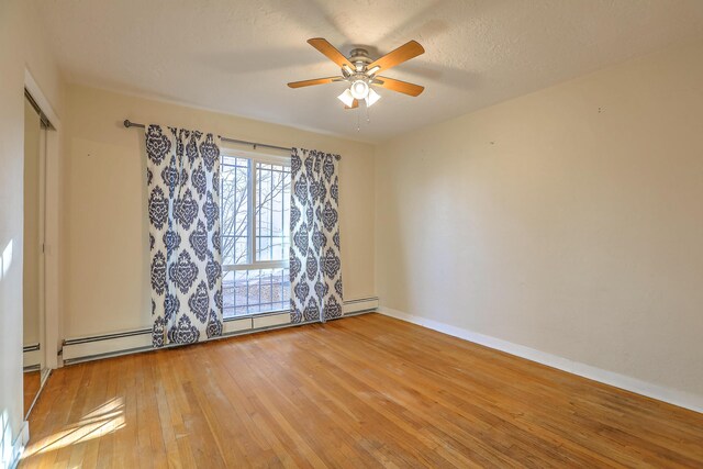 unfurnished room featuring baseboard heating, a ceiling fan, a textured ceiling, baseboards, and hardwood / wood-style flooring