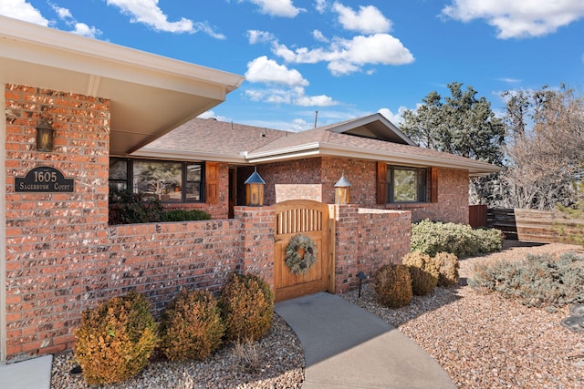 ranch-style house with a gate, fence, brick siding, and a shingled roof