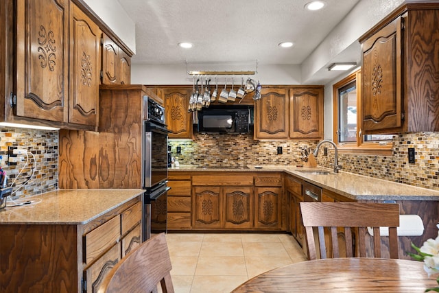 kitchen featuring tasteful backsplash, brown cabinets, light tile patterned flooring, black appliances, and a sink