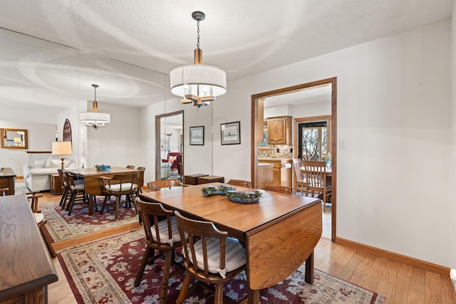 dining space with baseboards, a textured ceiling, and light wood finished floors