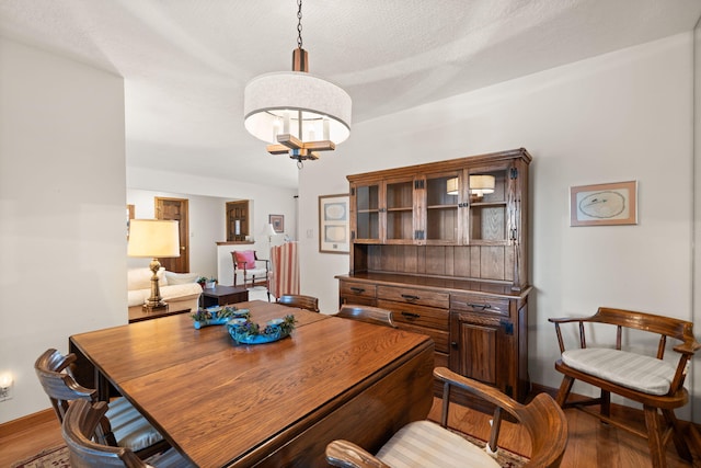 dining room with baseboards, a textured ceiling, an inviting chandelier, and wood finished floors