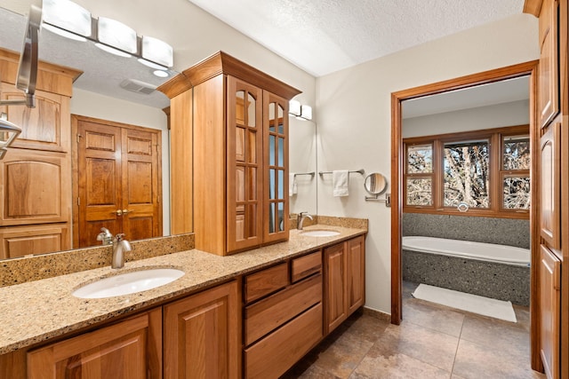 full bathroom with a textured ceiling, double vanity, a bath, and a sink