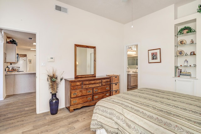 bedroom featuring ensuite bath, white refrigerator, and light wood-type flooring