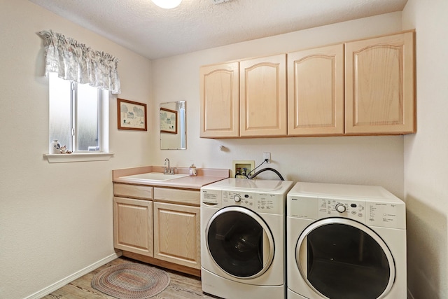 clothes washing area with sink, cabinets, a textured ceiling, independent washer and dryer, and light hardwood / wood-style floors