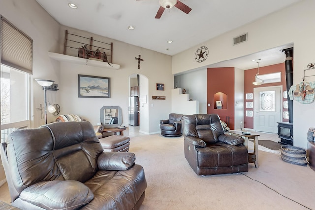 carpeted living room with a wood stove and ceiling fan