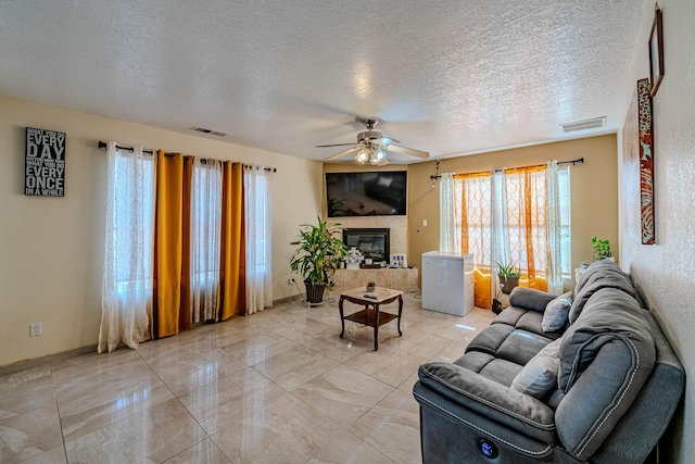 living room with ceiling fan, a tiled fireplace, and a textured ceiling