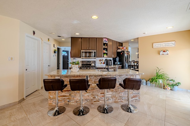 kitchen with a kitchen island with sink, sink, a breakfast bar area, and appliances with stainless steel finishes