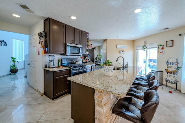 kitchen featuring dark brown cabinetry, stainless steel appliances, and a kitchen island with sink