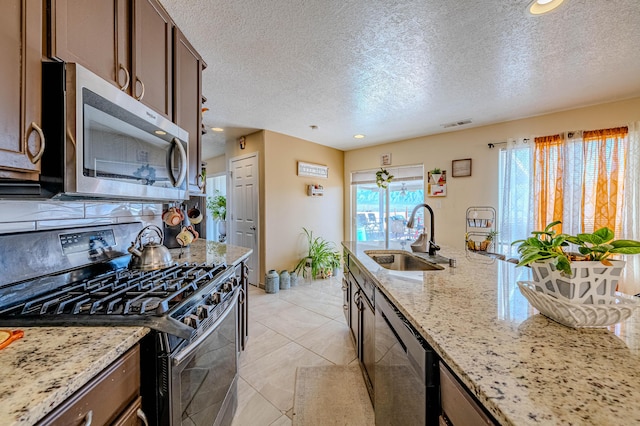 kitchen featuring sink, light tile patterned floors, stainless steel appliances, light stone countertops, and a textured ceiling