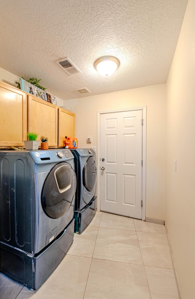 laundry area featuring a textured ceiling, cabinets, washing machine and clothes dryer, and light tile patterned flooring