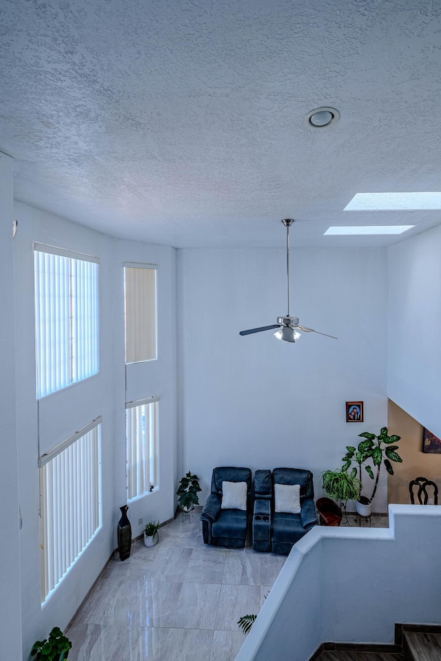 living room featuring ceiling fan, a towering ceiling, a skylight, and a textured ceiling