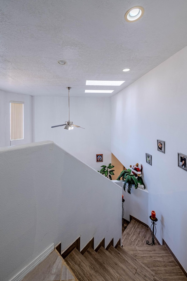 staircase with ceiling fan, hardwood / wood-style flooring, and a textured ceiling