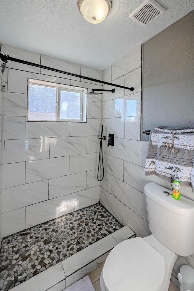 bathroom featuring a textured ceiling, toilet, and tiled shower