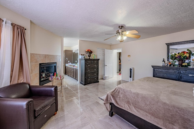 bedroom featuring a tiled fireplace, ceiling fan, and a textured ceiling