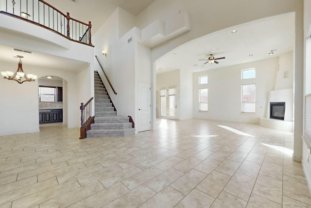 unfurnished living room featuring stairs, arched walkways, visible vents, a large fireplace, and ceiling fan with notable chandelier