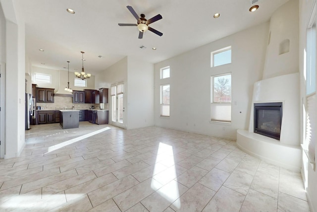 unfurnished living room featuring recessed lighting, a large fireplace, a towering ceiling, and ceiling fan with notable chandelier