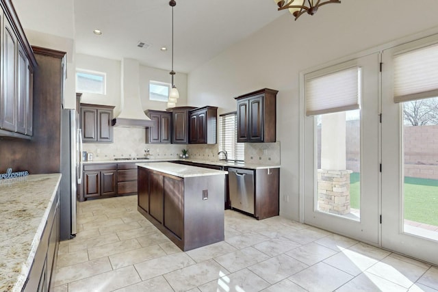 kitchen with dark brown cabinetry, decorative backsplash, a kitchen island, appliances with stainless steel finishes, and premium range hood